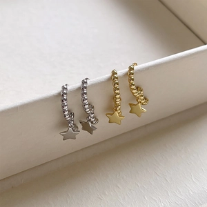 Macro shot of silver and gold beaded hoop earrings with matte star charms on beige box
