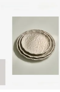 Detail of stacked cream ceramic plates with unique ripple texture and vintage artistic style