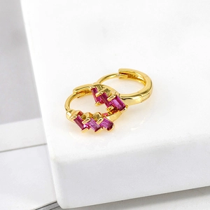 Macro shot of gold-plated huggie hoop earrings with rectangular pink zircon stones