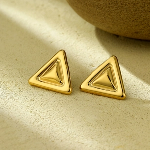 Macro shot of gold-plated stainless steel triangle stud earrings on a textured stone surface