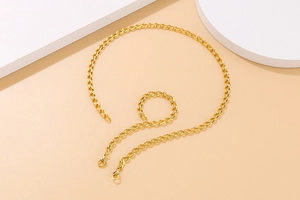 Goldenes Set aus gewebter Halskette und Armband in Herzform auf beigem Hintergrund drapiert