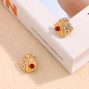 Detail of 18K gold scallop earrings with red stone and rhinestones on a summer book