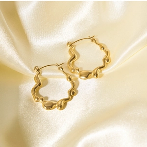 Detailed close-up of gold irregular wavy earrings resting on luxury beige silk fabric