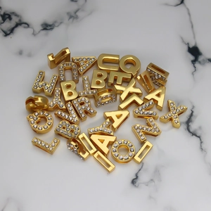 Close-up of gold rhinestone alphabet charms on marble surface for DIY jewelry making