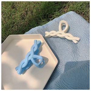 Blue and white matte plastic hair claws in twisted wave design on a tray and grass