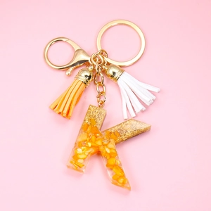 Macro shot of resin letter K keychain with orange stones, gold ring and fringe tassel