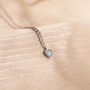 Macro shot of light blue heart-shaped opal pendant with polished silver chain detail
