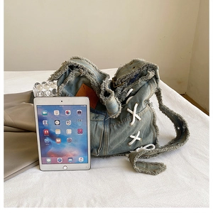 Detail of washed denim bag with raw edges and criss-cross rope ties next to an iPad