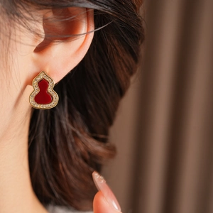 Detailaufnahme eines vergoldeten Kürbis-Ohrrings mit roter Emaille und Zirkon am Modell