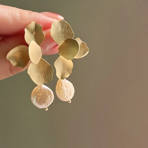 Macro shot of gold petal flower earrings with baroque pearls held by fingers