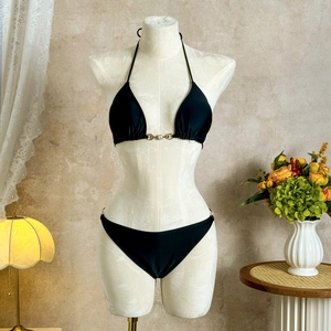 Close-up of black bikini with gold metal ring and pearl details on white mannequin