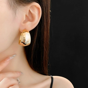 Detailed view of wide C-shaped gold earrings with hammered metal texture on model