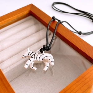Detailed close-up of a zebra pendant necklace with white enamel and black wax cord