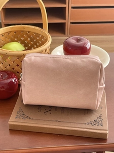 Pink waterproof PU cosmetic bag with zipper placed on books in a warm home setting