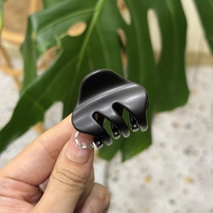 Detailed close-up of matte black cloud hair claw clip held by hand in natural light