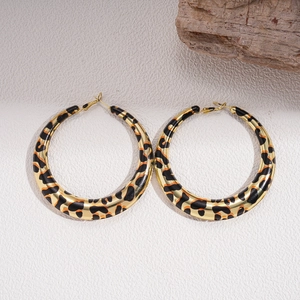 Detail of gold leopard print geometric hoop earrings on textured beige stone
