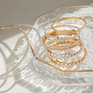 Macro detail of gold and silver layered bracelets with sparkling zircons in a glass tray