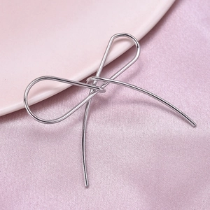 Detailed view of a silver stainless steel bow pendant on soft pink silk fabric