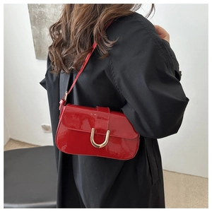 Rear view of a red patent leather shoulder bag with a gold buckle on a model