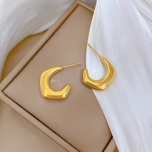 Detailed close-up of golden irregular geometric hoop earrings on soft white fabric