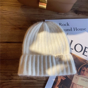 Detailed close-up of a cozy cream knit beanie with 1982 California embroidery on a wooden table