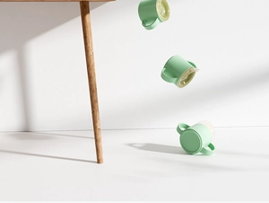 Three green silicone baby cups with dual handles falling in the air on white backdrop
