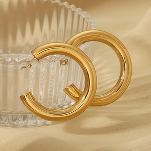 Gros plan de boucles d'oreilles créoles dorées sur un verre sur fond beige doux
