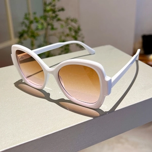 Detail view of white wide-frame sunglasses with orange gradient lenses on a grey surface