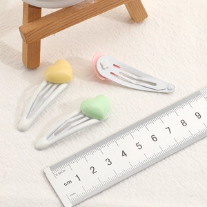 Set of three colorful heart-shaped hair clips for girls on a textured beige background
