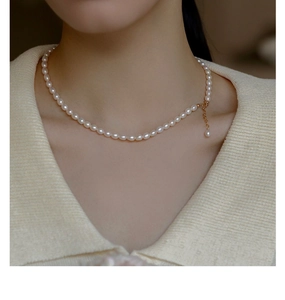 Close-up of a cream white freshwater pearl necklace with adjustable gold clasp on a model