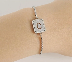 Detailed view of silver square letter C pendant on a box chain worn on the wrist