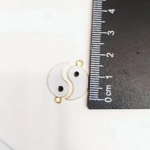 Close-up of white Tai Chi Yin Yang charms with gold borders next to a measuring ruler