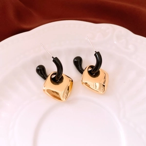 Detail of geometric earrings with black C-shape and gold diamond-shaped metal pendant