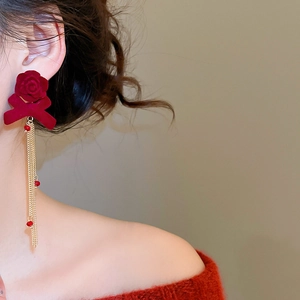 Close-up of elegant burgundy flocked rose and bow earrings with long golden tassels