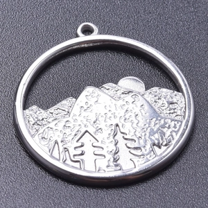 Macro shot of silver stainless steel pendant with embossed mountain and tree scenery