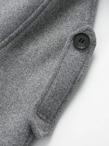 Detail of grey wool coat featuring a dark amber button and textured side pocket seam