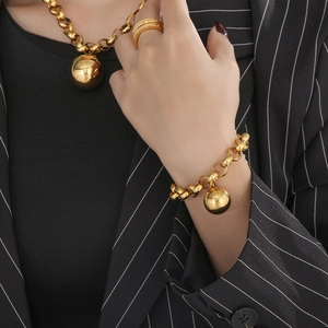 Close-up of a polished gold jewelry set featuring spherical charms and a wide band ring