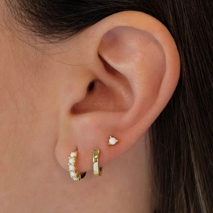 Close-up of gold ear stack featuring hoop earrings and studs with white opal inlay
