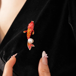 Macro detail of red enamel koi fish brooch with a white pearl on black velvet fabric