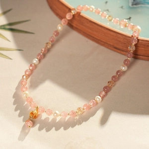 Detail of strawberry quartz necklace with freshwater pearls and a gold bell charm