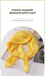 Detail of a pleated lemon yellow silk scarf folded elegantly on a white tray