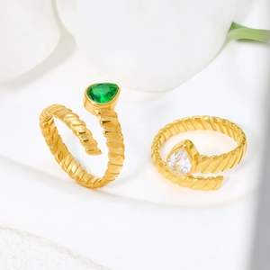 Detail of gold spiral open rings with green and clear pear-shaped crystals on white surface