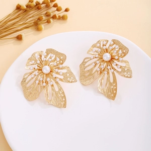 Detailed view of vintage gold hollow flower earrings with white pearls on a white plate