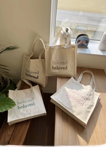 Detail of embroidered lettering on cream canvas tote bag in multiple color variations