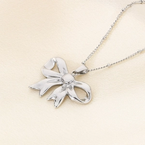 Close-up of a silver hollow bowknot pendant with a metallic luster on textured fabric