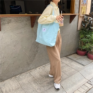 Close-up of a light blue canvas tote bag with a white square patch on an outdoor street