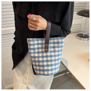 Close-up of a blue checkered canvas bucket bag with brown leather handles held by a model