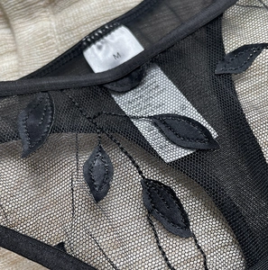 Close-up of black mesh thong featuring detailed leaf embroidery and a white size M label