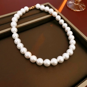 Détail de perles blanches rondes avec fermoir doré sur un plateau à bijoux marron