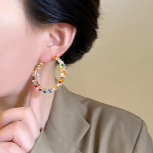 Close-up of colorful crystal bead wrapped hoop earrings on a model with warm tones